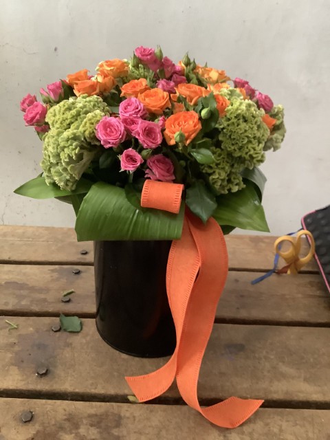 Flower Arrangement with vibrant orange and pink roses paired with green celosia in a black metalic container